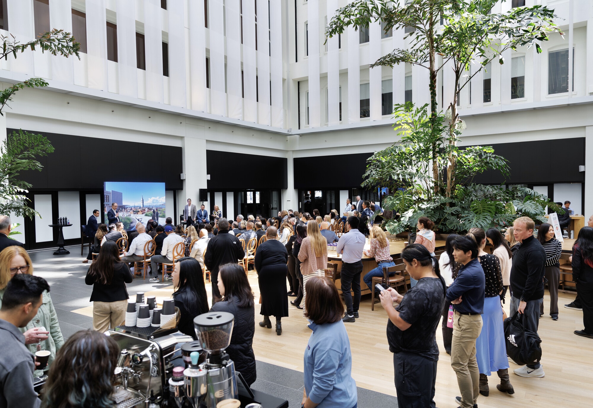 An event in the One Market Plaza atrium: a coffee bar, a crowd, and a presentation under the trees